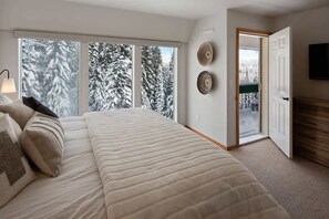 Quarto com uma cama grande, uma janela com vista para árvores cobertas de neve e uma porta que dá para uma varanda.