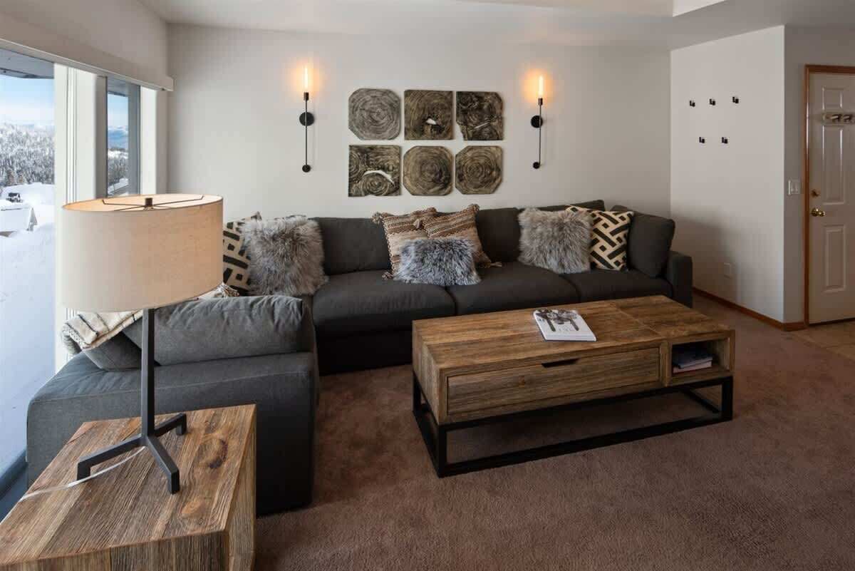 A modern living room with a grey sofa, a wooden coffee table, and a lamp. There are wall-mounted art pieces and two wall sconces.