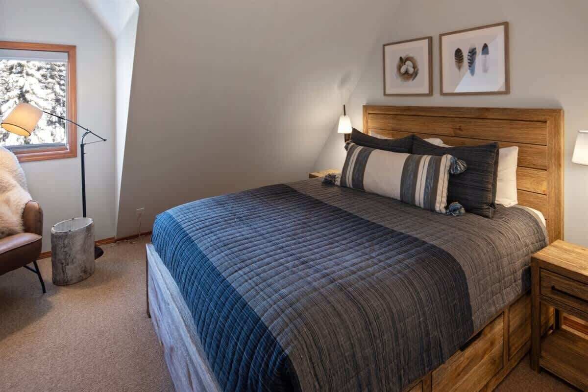 A bedroom with a large bed, wooden headboard, and a nightstand. There is a chair and a lamp in the corner.