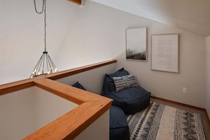 Uma sala de estar moderna com uma mesa de centro de madeira, um sofá azul escuro com almofadas estampadas, um lustre pendente e um texto emoldurado na parede.