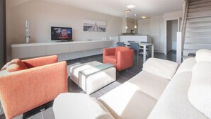 A modern living room with a sofa, armchair, and ottoman. There is a television on a stand and a dining area with chairs and a table. - Skyview with parking and balcony by Interhome (Blankenberge)