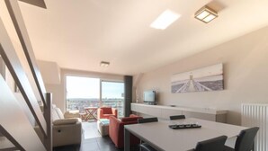 A modern apartment with a dining area, a TV, and a city view. - Skyview with parking and balcony by Interhome (Blankenberge)