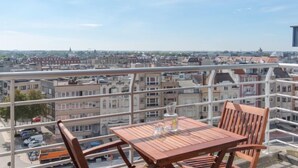 A balcony with a table and chairs, overlooking a cityscape with buildings and a clear sky. - Skyview with parking and balcony by Interhome (Blankenberge)