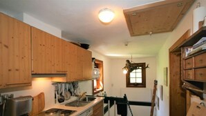A compact kitchen with wooden cabinets, a stove, a sink, and a hanging light fixture. - Vogelhütte by Interhome (Innsbruck)
