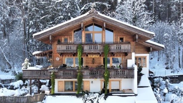 Een meerlaags houten chalet met balkons, omgeven door sneeuwtakels.