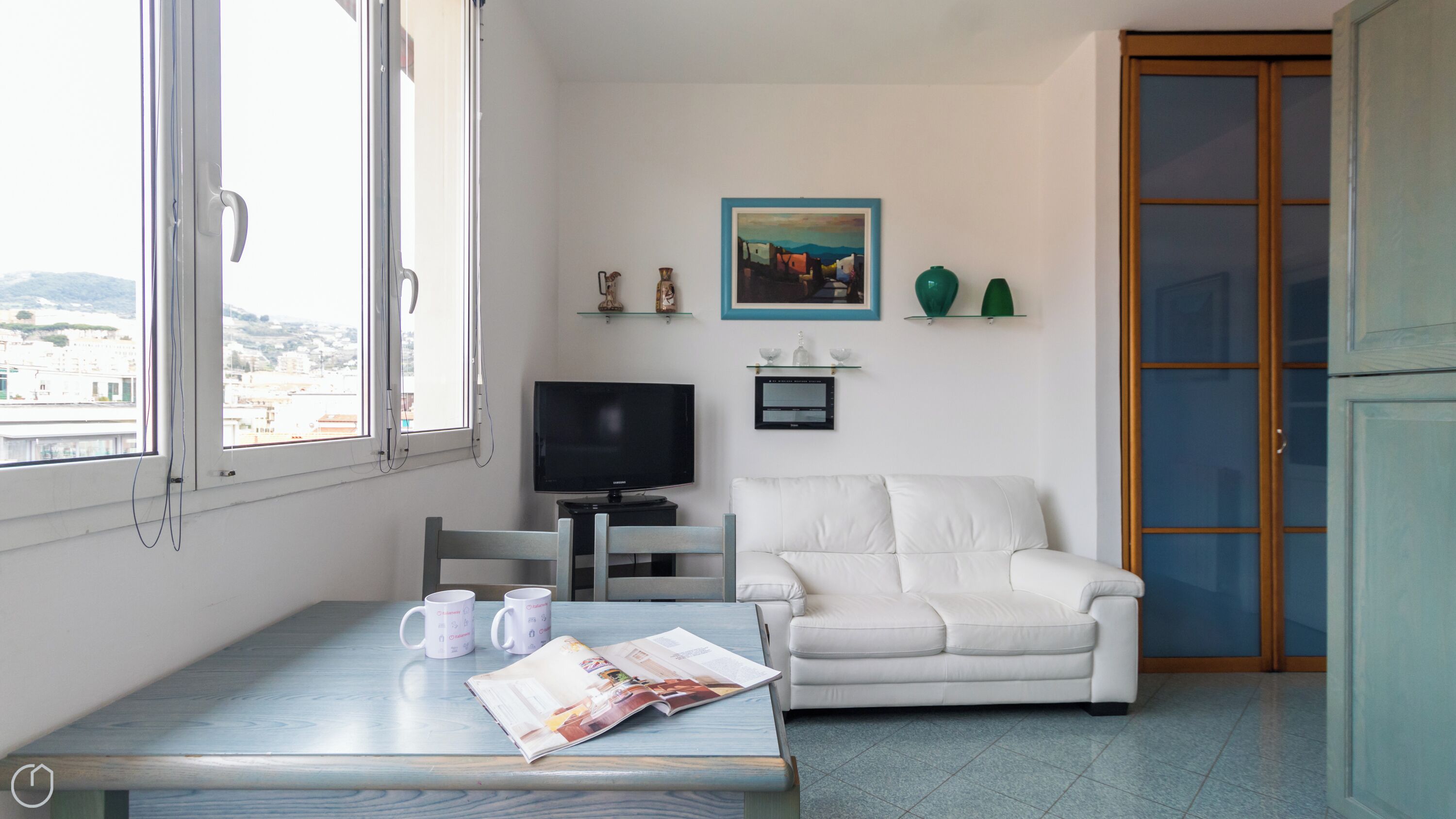 Ein Wohnzimmer mit einem weißen Sofa, einem Fernseher und einem Tisch mit zwei Tassen und einer Zeitschrift.
