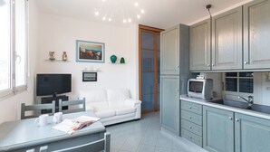 A compact living space with a sofa, television, dining table, and kitchenette. - Italianway - Roma 70 (Sanremo)