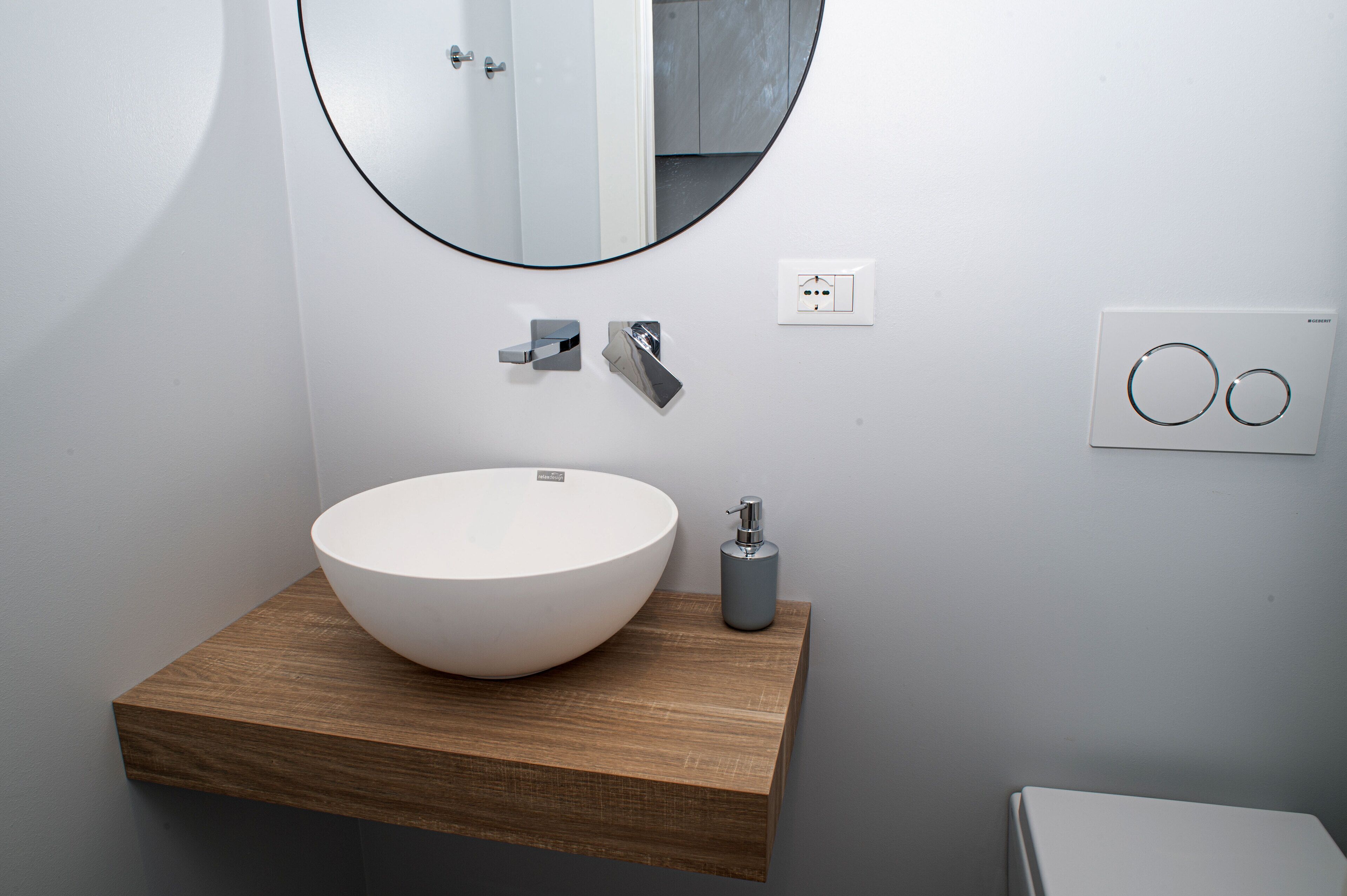 Une salle de bain moderne avec un meuble-lavabo en bois, un grand lavabo blanc, un miroir rond et des toilettes.