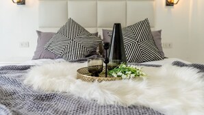 A bed with a tufted headboard, patterned pillows, a glass of drink, and a decorative tray with flowers.