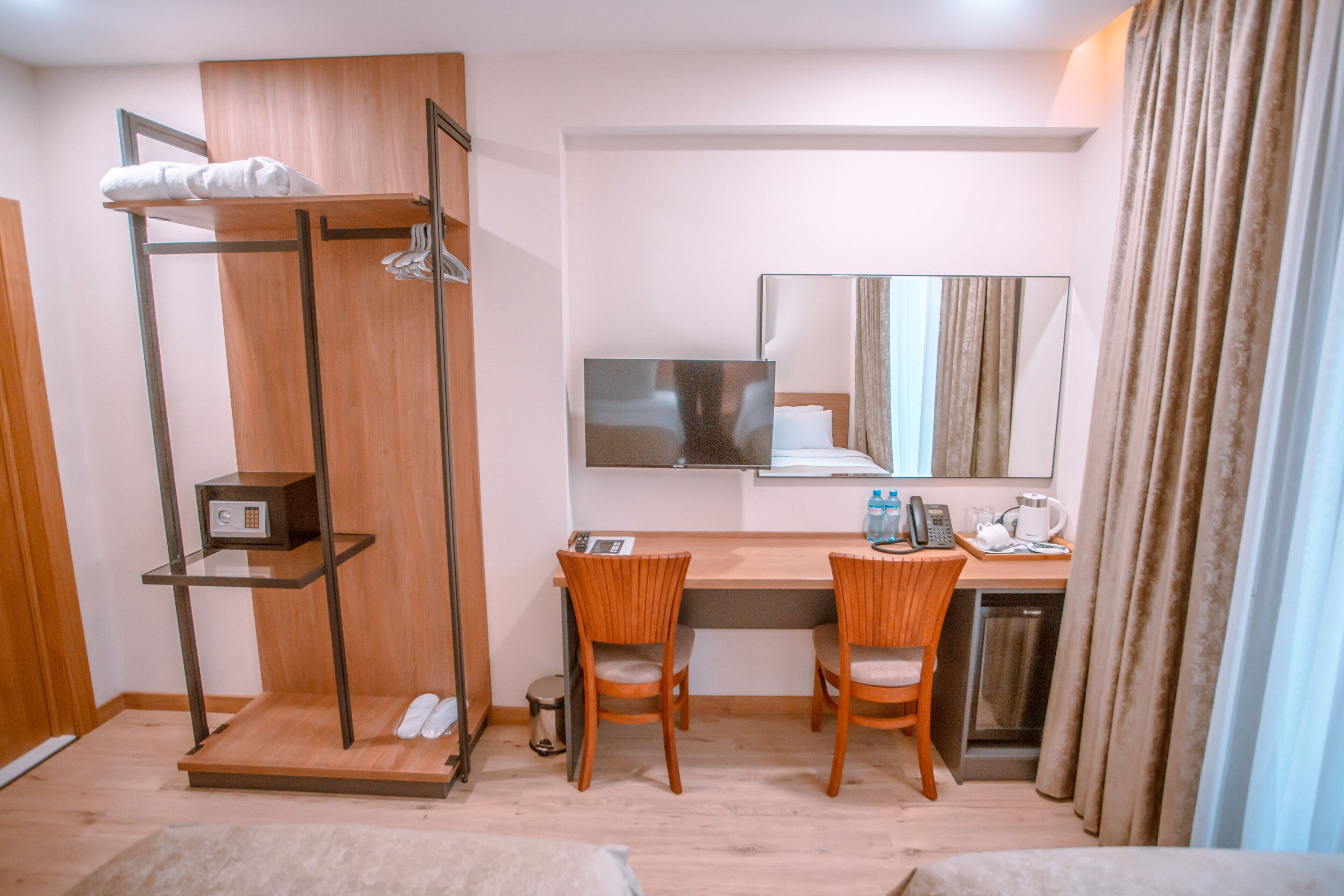 Camera d'albergo compatta con una scrivania in legno, due sedie, un piccolo ripiano con un asciugamano, uno specchio e una televisione.