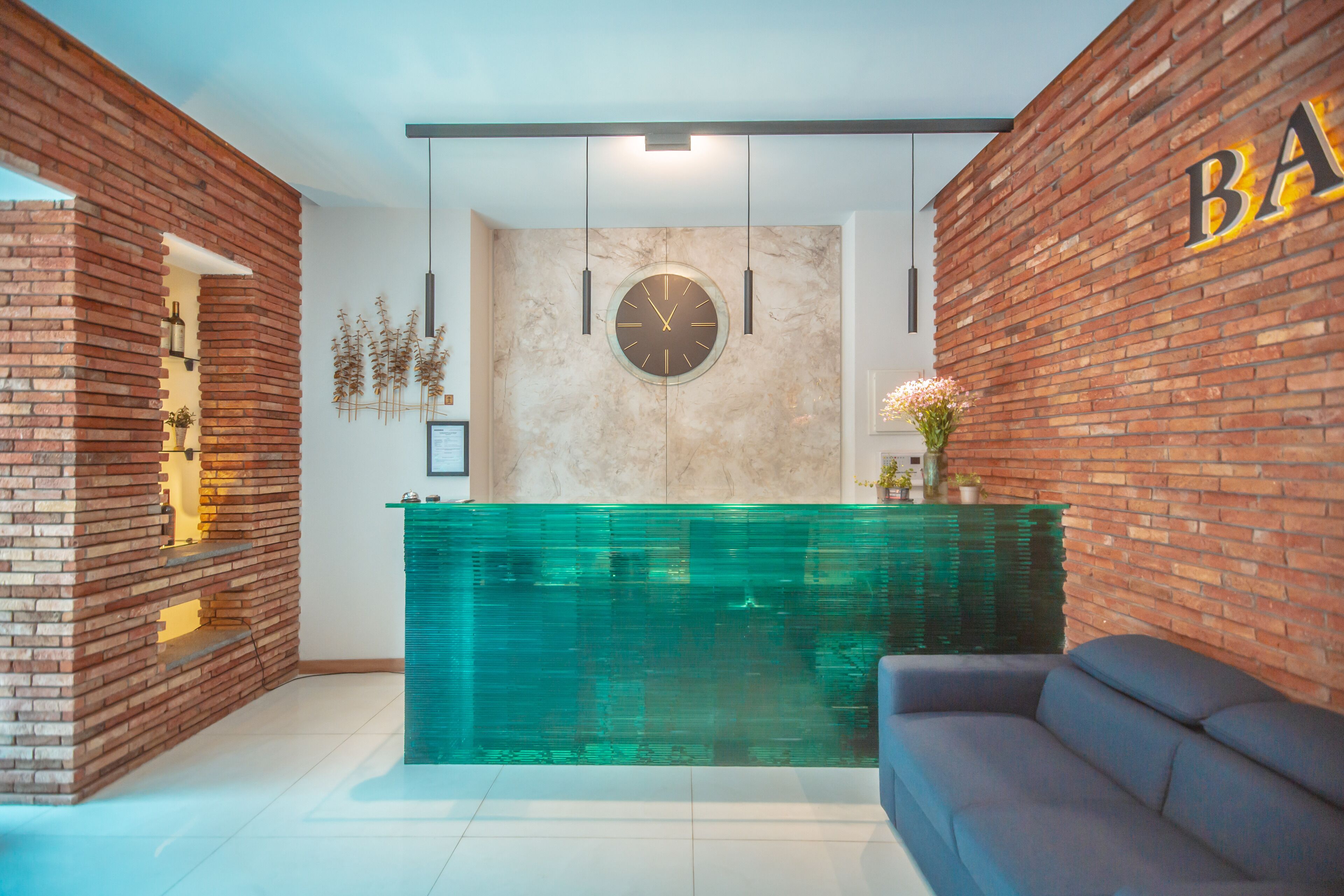 A reception area with a brick wall, a clock, hanging lights, and a sofa.