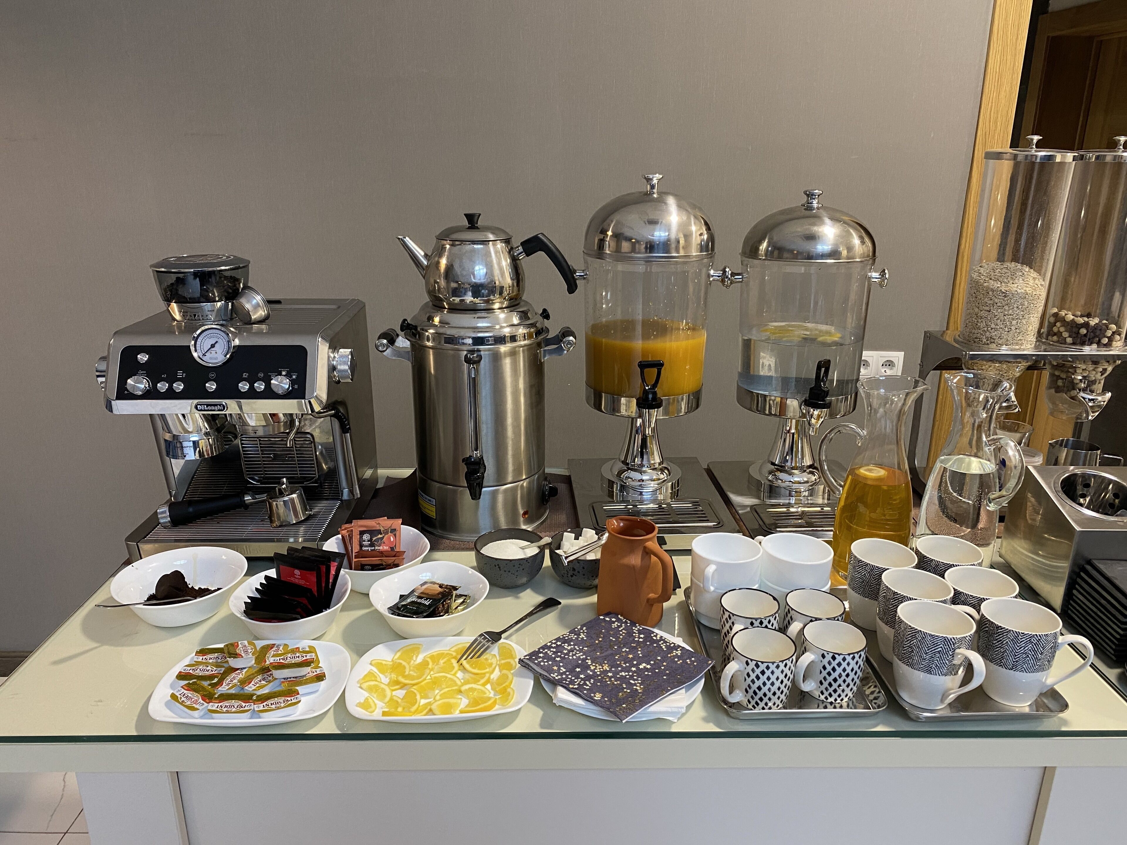 A breakfast buffet with coffee machines, a coffee press, and various food items on a glass table.