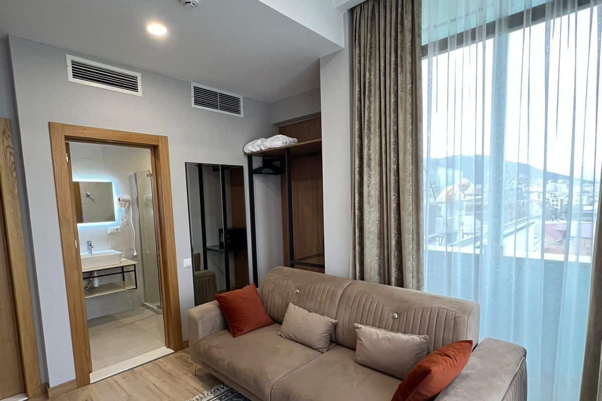 A modern living room with a beige sofa, patterned rug, and a view of the city through large windows.
