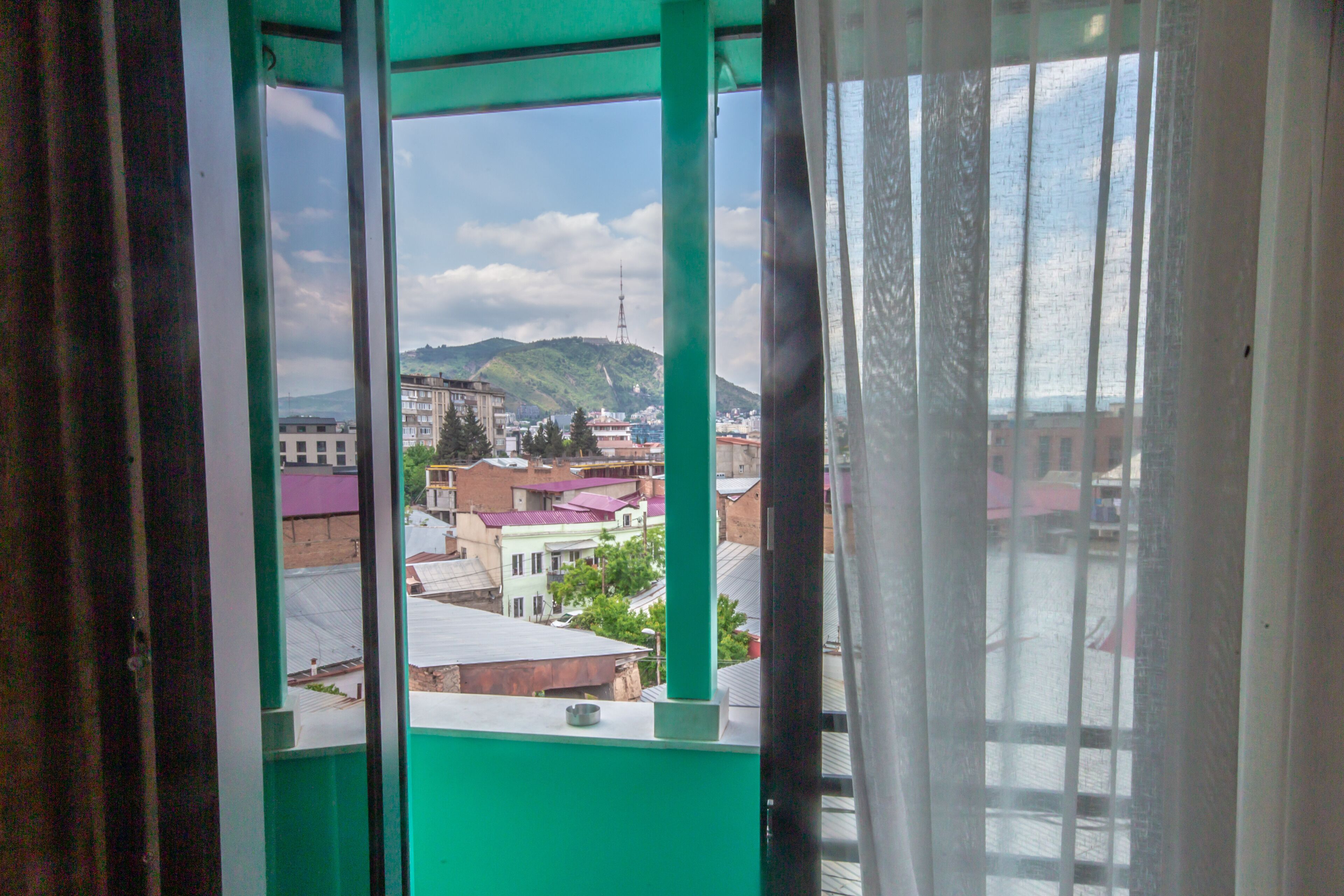 Blick aus einem Fenster mit grünem Rahmen auf Gebäude und einen Hügel mit einem Turm.