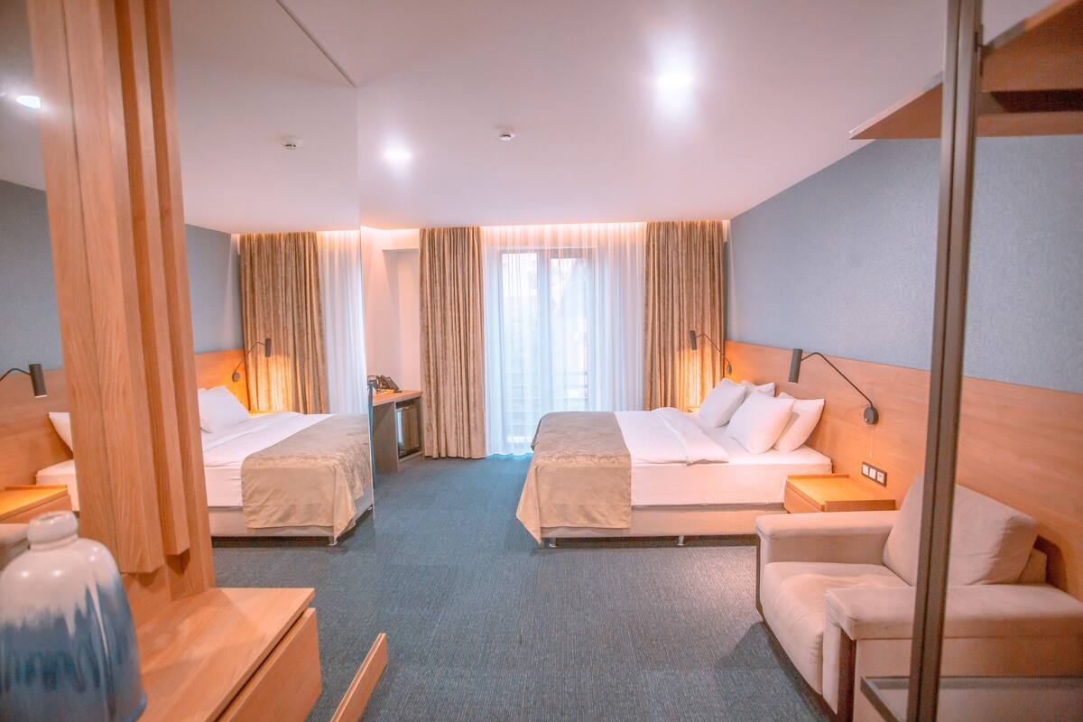 A hotel room with two beds, a desk, a chair, and a large window with curtains.