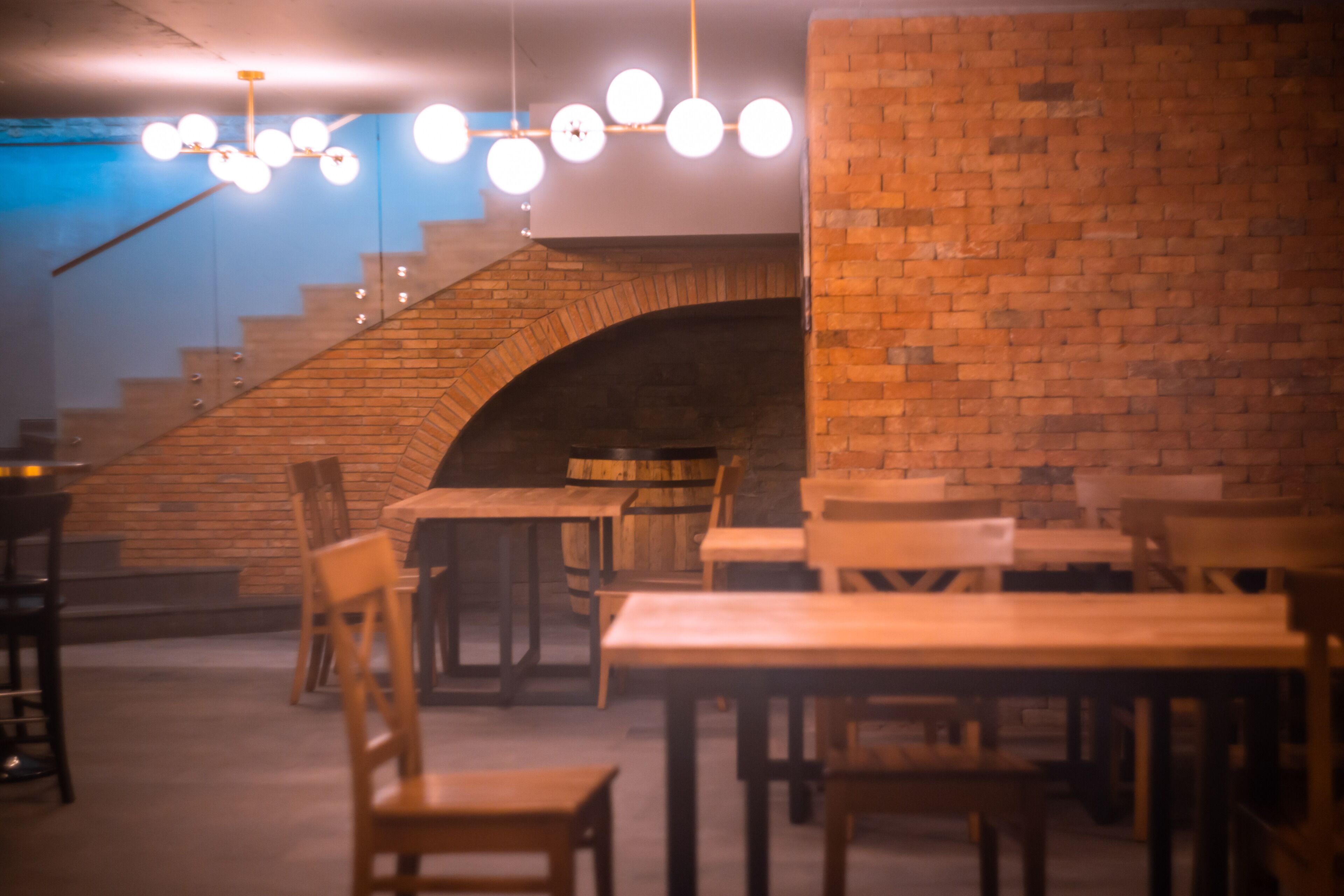 A restaurant with brick walls, wooden tables, and hanging spherical light fixtures.