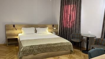 Une chambre d’hôtel avec un lit en bois, une petite table ronde, une chaise et un appareil de climatisation.