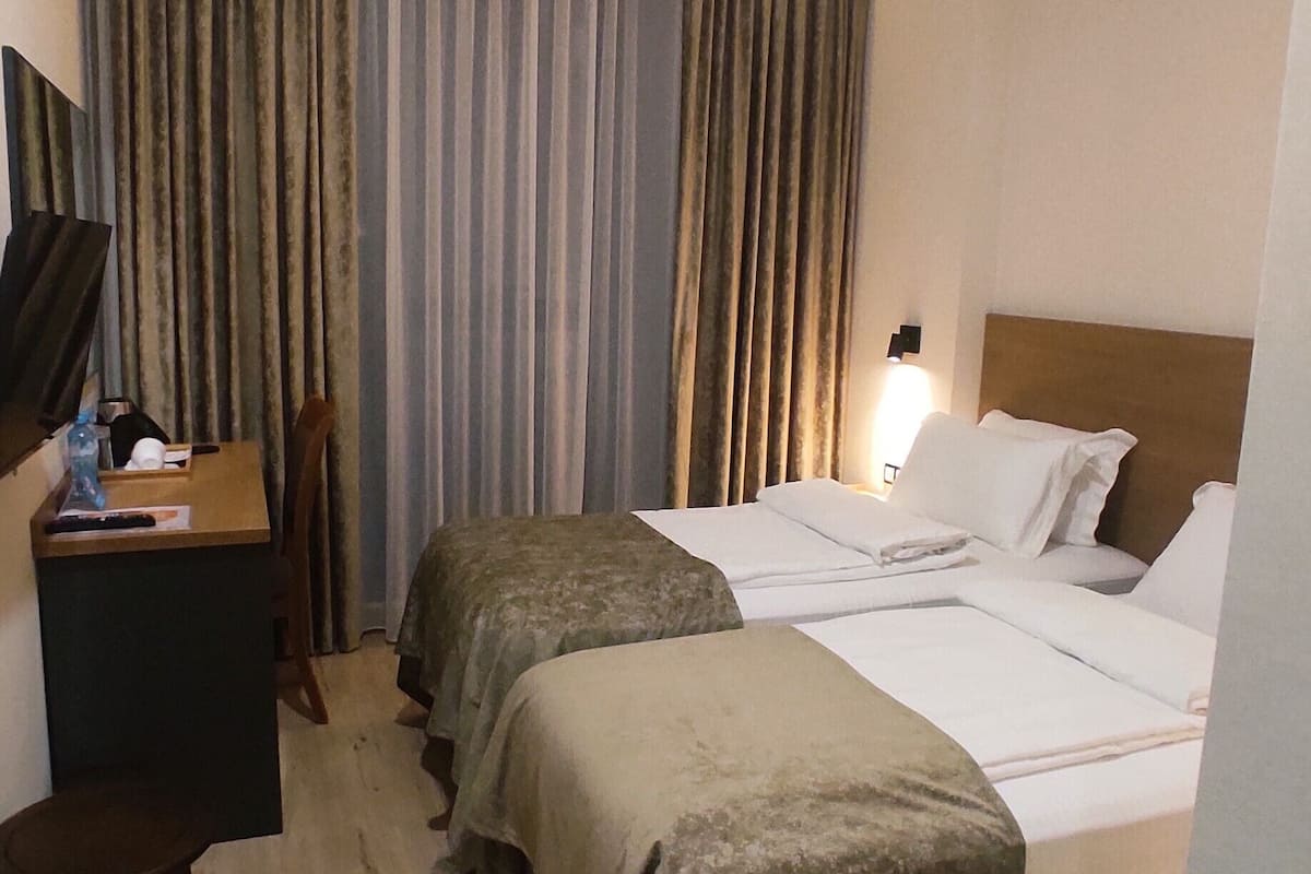 A hotel room with two beds, a desk, a chair, and a large window with curtains.