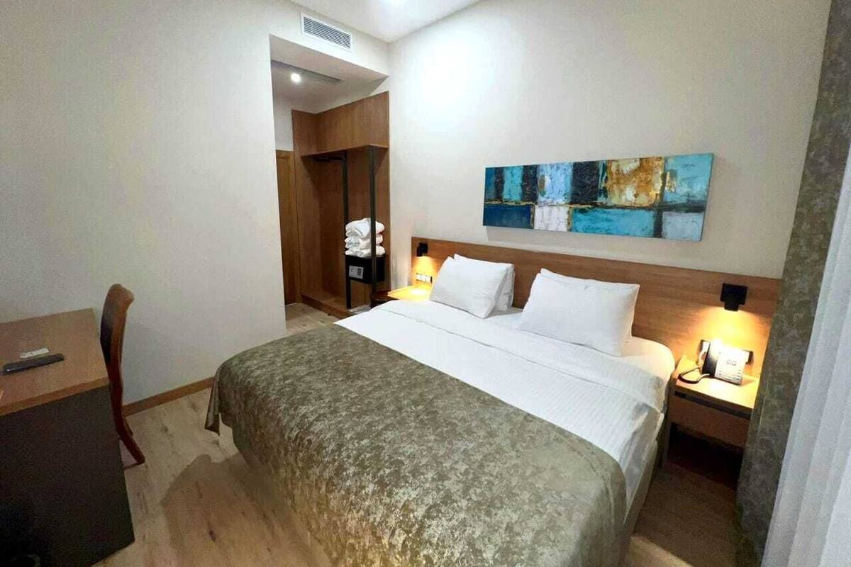 A hotel room with a bed, bedside tables, a desk, and a wardrobe.