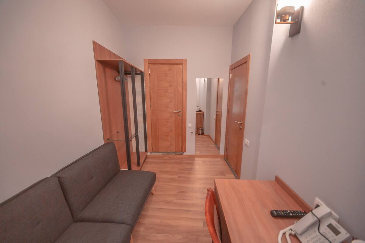 A hotel room with a wooden floor, a sofa, a table, and a remote control on the table.