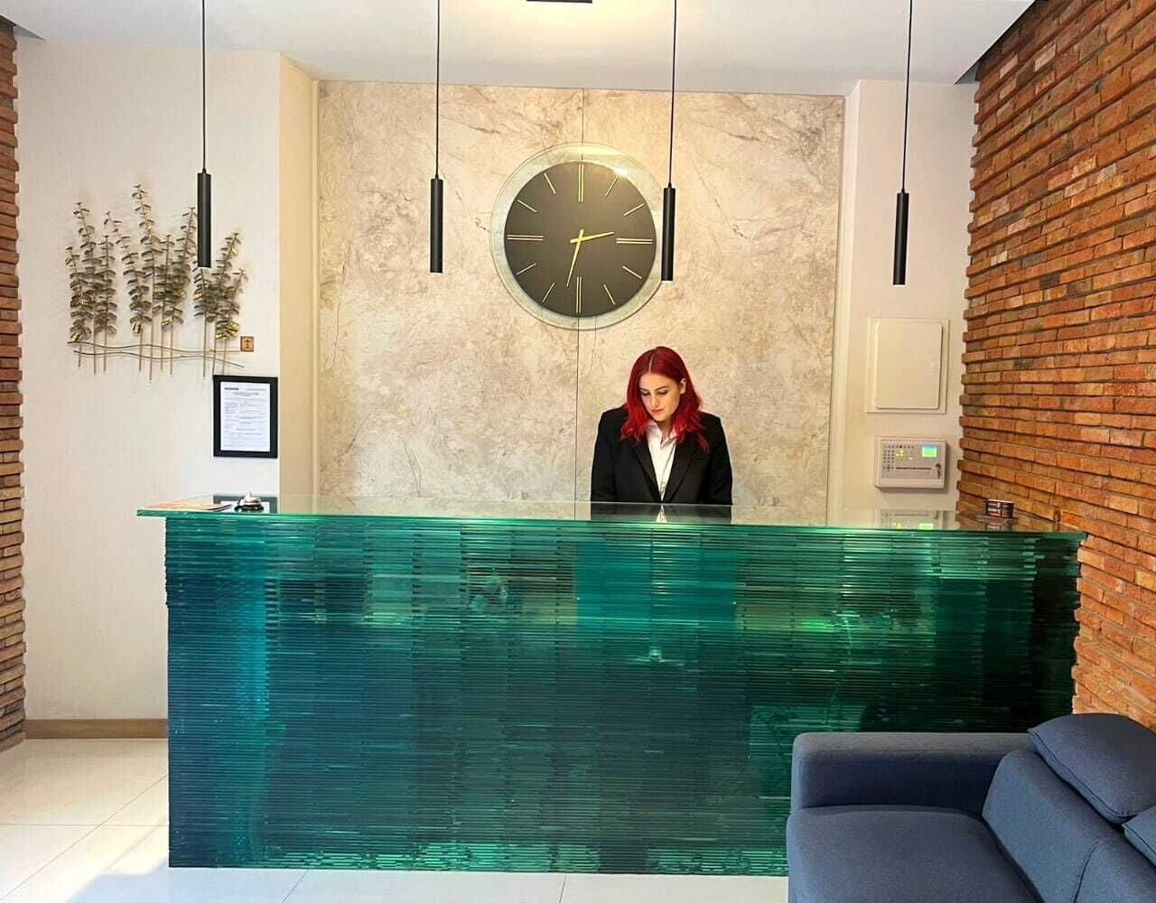A reception area with a modern design, featuring a glass reception desk, a large wall clock, and a brick accent wall.