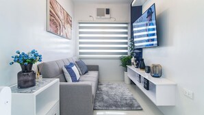 A modern living room with a grey sofa, a flat-screen TV, a decorative vase with blue flowers, and a grey rug.