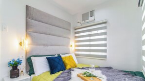 A modern bedroom with a bed, bedside table, and a window with blinds.