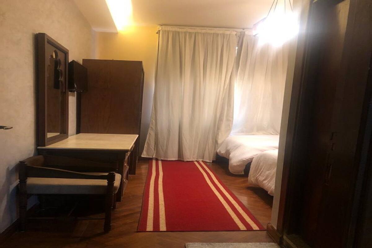 Una habitación pequeña con una cama, una mesita, una silla y un tapete a rayas rojo y blanco.