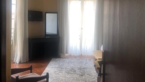 Una habitación con televisión, una silla de madera, una mesita y una ventana con cortinas.
