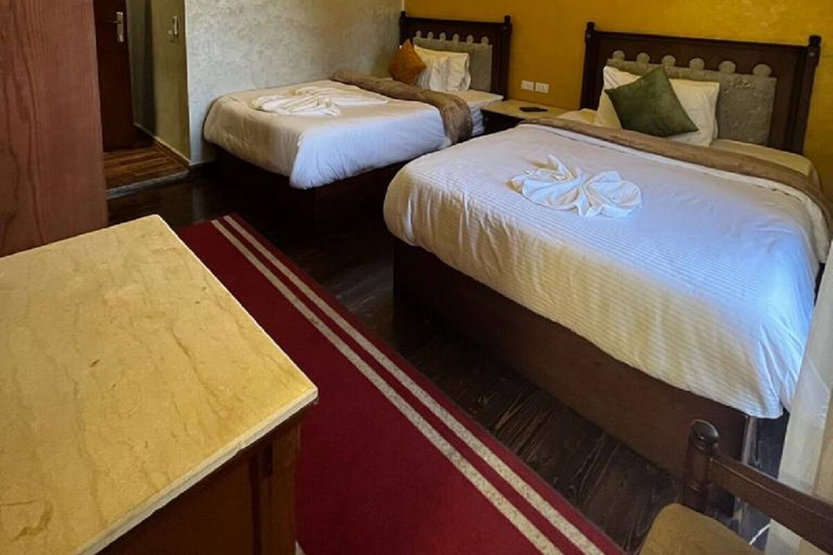 Habitación de hotel con dos camas, una mesita y una alfombra roja.
