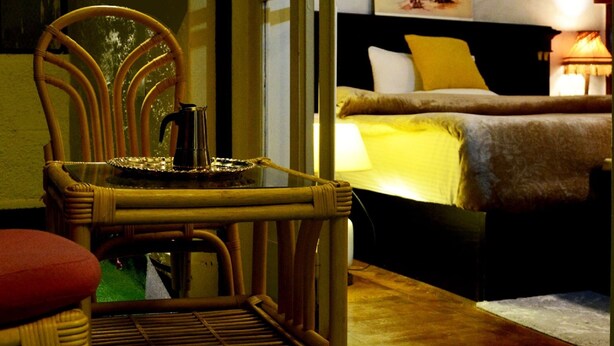 Una habitación con una silla de mimbre, una cama con una manta amarilla y una lámpara.