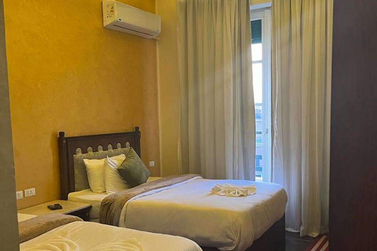 Habitación de hotel con dos camas, alfombra roja y una ventana con cortinas.