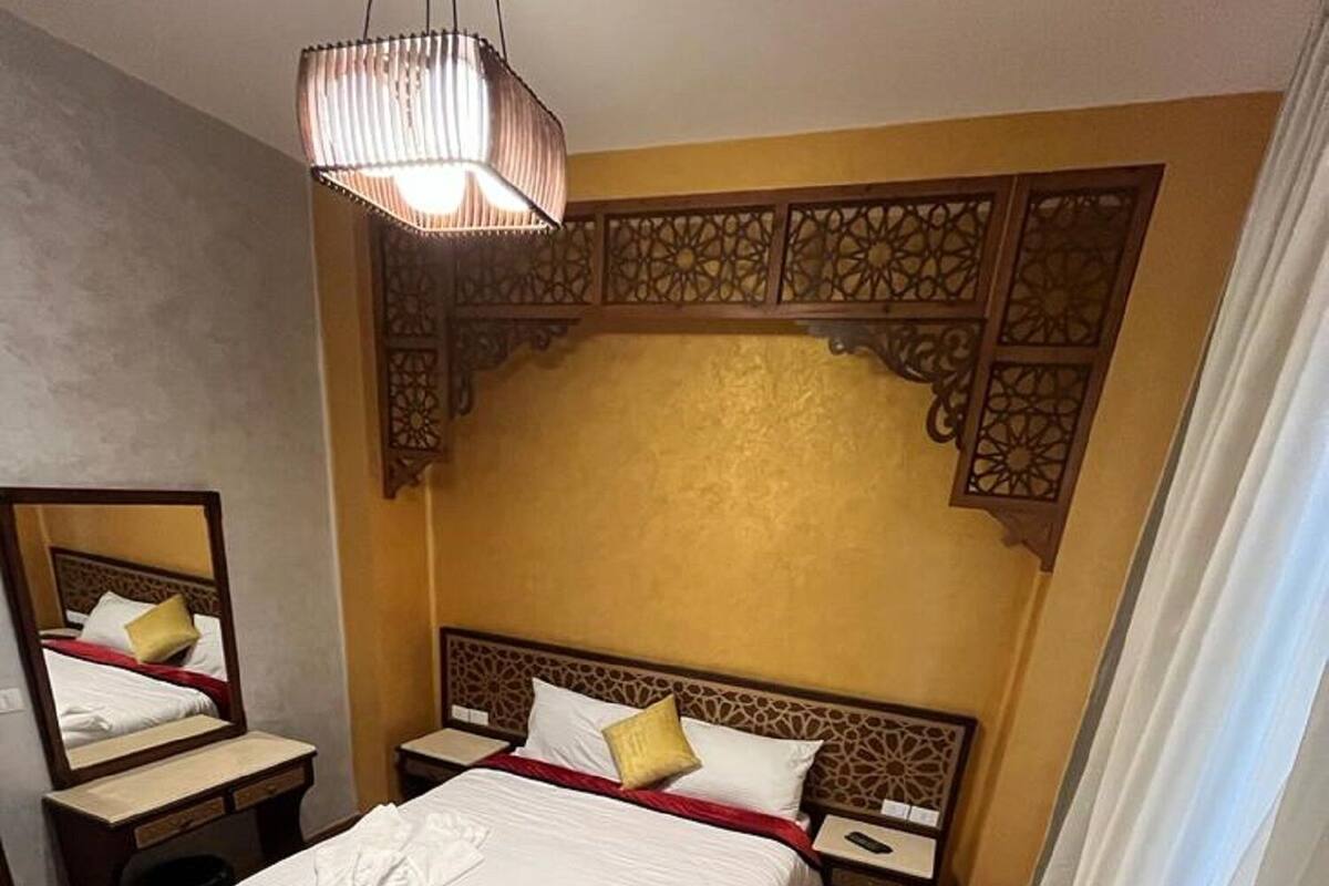 Habitación de hotel con una cama grande, una mesita de noche, un espejo y una lámpara colgante.