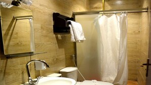 Un baño con suelo de madera, lavamanos, inodoro y cortina de ducha.