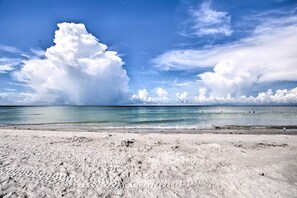 Uma praia com céu claro e grandes nuvens.