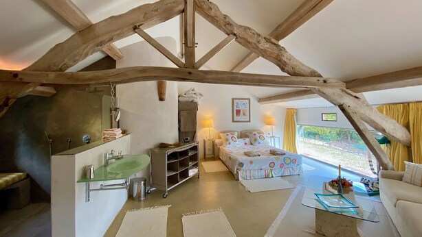 Un interior rústico con vigas de madera a la vista, una kitchenette, una cama con ropa de cama colorida y vistas al exterior.