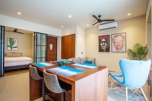Una habitación de hotel moderna con una mesa de comedor de madera, dos taburetes altos, un ventilador de techo y un ventanal grande.