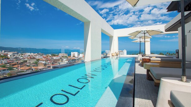 Una piscina infinita con vista a la ciudad, mobiliario exterior y sombrillas.