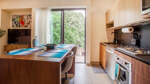 Una cocina moderna con comedor, televisor y un amplio ventanal con vistas a árboles.