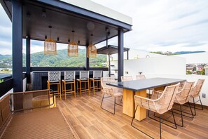 An outdoor patio with a dining area, wicker chairs, and a view of the landscape. - Modern 2BR Near Beach & Boardwalk | Gym & BBQ (Puerto Vallarta)