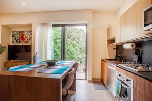 A modern kitchen with a dining area, a large window, and a view of greenery outside. - Modern 2BR Near Beach & Boardwalk | Gym & BBQ (Puerto Vallarta)
