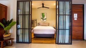Un dormitorio con cama, ventilador de techo, planta y puerta de madera.