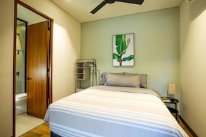 Un dormitorio con cama, mesita de noche, lámpara y estante en la pared.