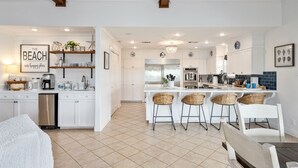 A modern kitchen with white cabinetry, a central island with bar stools, and a dining area with a white table and chairs.