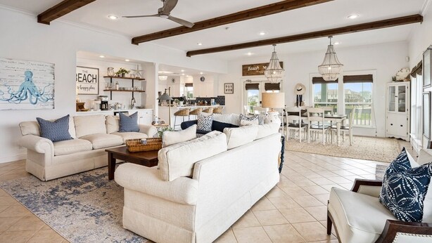 A spacious living room with a large sofa set, a dining area with a chandelier, and a kitchen in the background.
