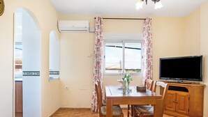 Ein Essbereich mit Tisch, Stühlen, einem Fernseher und einem Fenster mit Vorhängen.