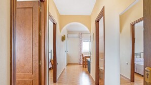 Ein Korridor mit Holztüren, Fliesenboden und einem Rundbogen, der zu einem Zimmer mit Bett und Bad führt.