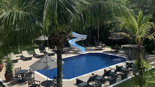 A pool area with a blue slide, lounge chairs, and palm trees. - Delta Maresias Club by SmartSharing (São Sebastião)