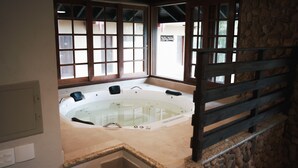 A spa room with a hot tub, stone walls, and a wooden railing. - Delta Maresias Club by SmartSharing (São Sebastião)