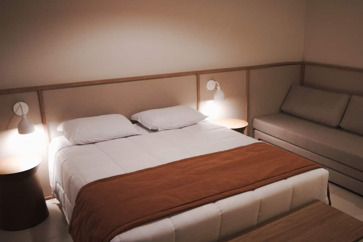 Quarto com cama, duas mesas de cabeceira, um criado-mudo e um sofá.